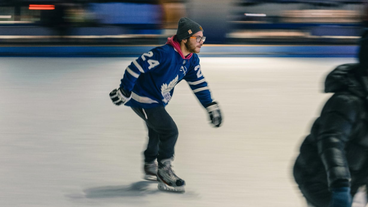 A blurry action photo of someone skating. They are wearing winter clothes and a Toronto Maple Leafs jersey.